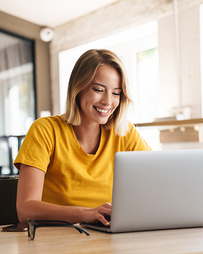 Photo of joyful nice woman using laptop and smiling while sitting at table