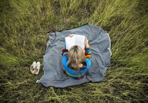 Girl sits in field reading book while benefitting from schizophrenia therapy in MA
