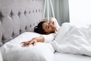 Woman waking up in bed stretches and smiles while enjoying the morning sunlight.
