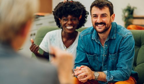 Portrait of a diverse couple smiling while trying to solve some issues in their relationship. Multiracial spouses talking in front of a therapist. Marital Therapy. Finding a solution. Copy space.